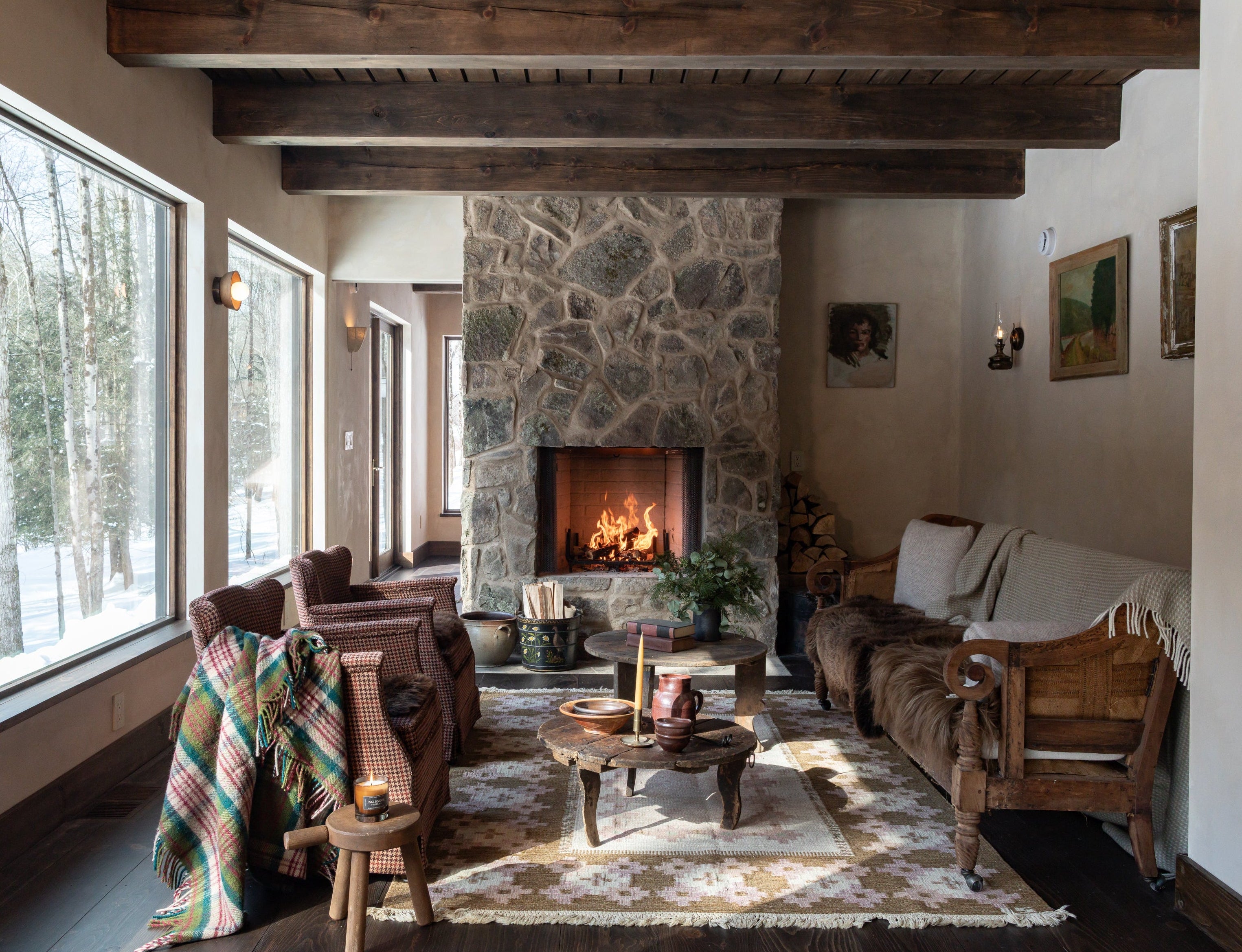 Living room with stone fireplace, exposed wood beam ceiling, and large windows, featuring natural materials and warm wood tones.
